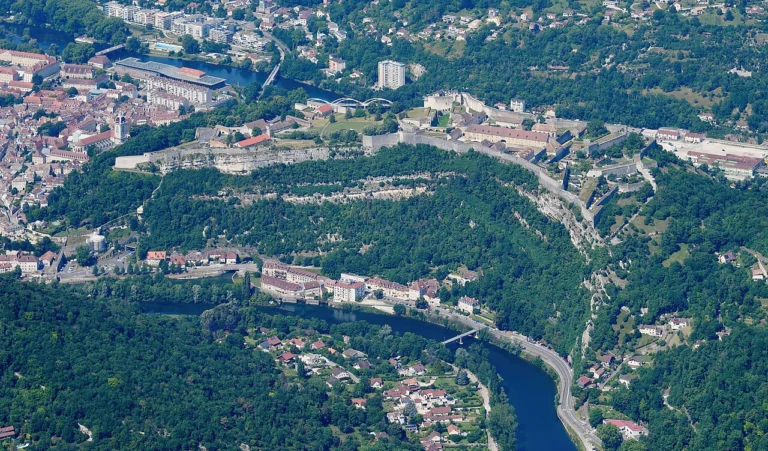 Vue aérienne d'une vaste forteresse sur une colline boisée, entourée par une rivière et par les quartiers de la ville.