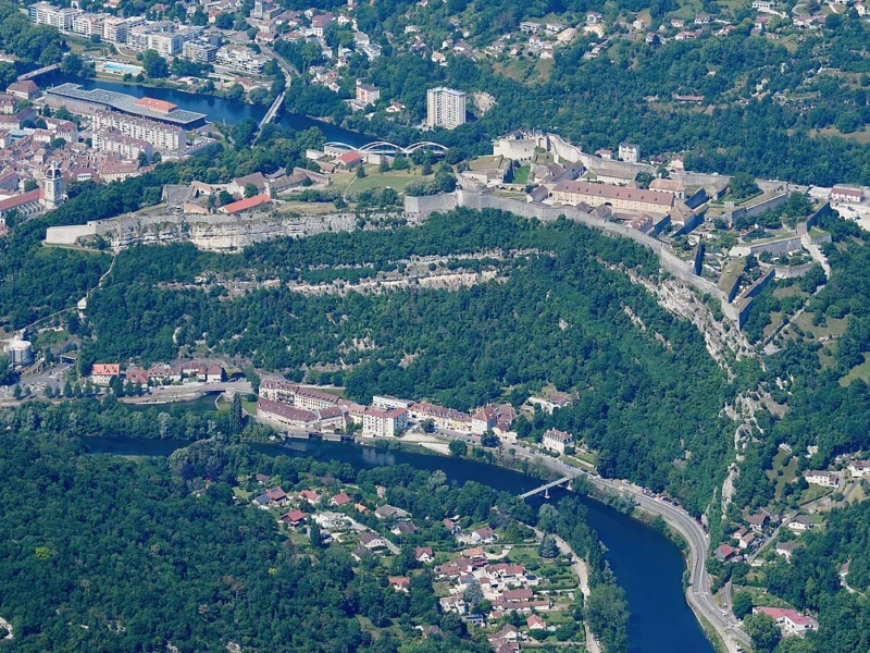 Vue aérienne d'une vaste forteresse sur une colline boisée, entourée par une rivière et par les quartiers de la ville.