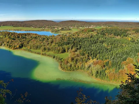 Vue panoramique sur plusieurs lacs bleus entourés de forêts aux couleurs d'automne et de prairies.