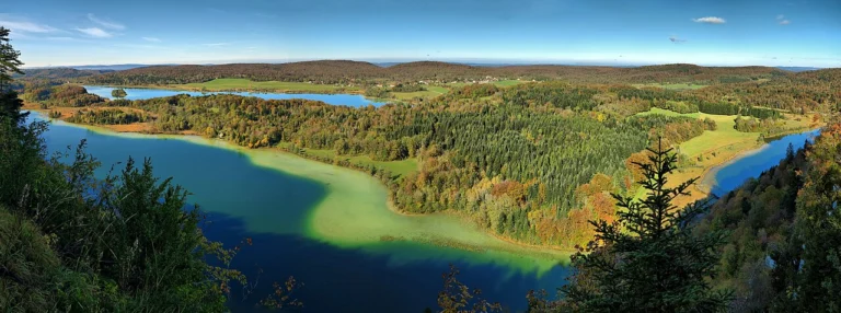 Vue panoramique sur plusieurs lacs bleus entourés de forêts aux couleurs d'automne et de prairies.