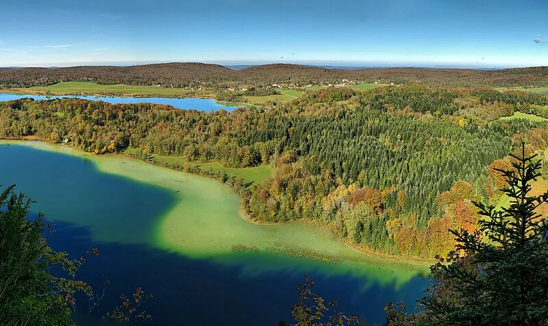 Vue panoramique sur plusieurs lacs bleus entourés de forêts aux couleurs d'automne et de prairies.