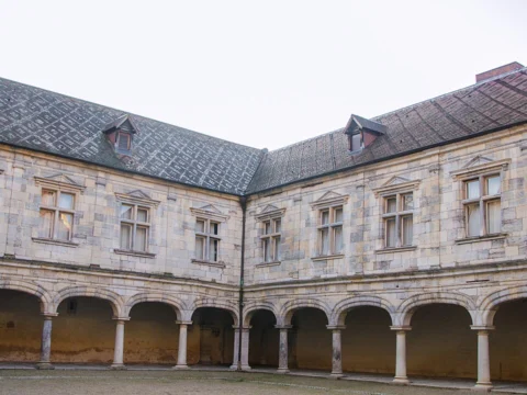 Cour intérieure d'un palais Renaissance en pierre claire, bordée d'une galerie à arcades sous un toit d'ardoise.