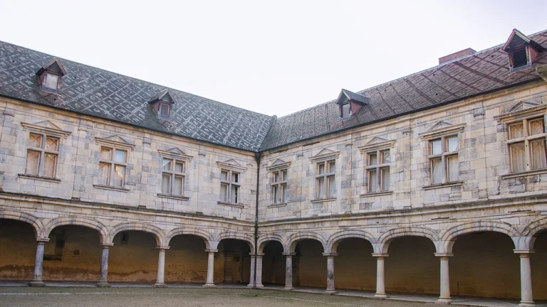 Cour intérieure d'un palais Renaissance en pierre claire, bordée d'une galerie à arcades sous un toit d'ardoise.