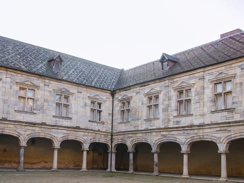 Cour intérieure d'un palais Renaissance en pierre claire, bordée d'une galerie à arcades sous un toit d'ardoise.