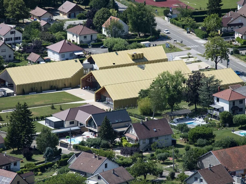 Vue plongeante sur un quartier résidentiel avec, au centre, un grand bâtiment aux toits clairs entouré de verdure.
