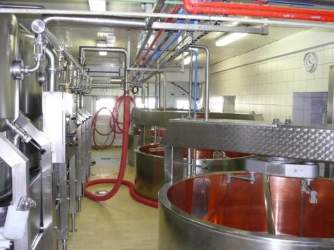 Salle de fabrication carrelée de blanc avec plusieurs cuves ouvertes à l’intérieur en cuivre, des tuyauteries et des équipements en inox.