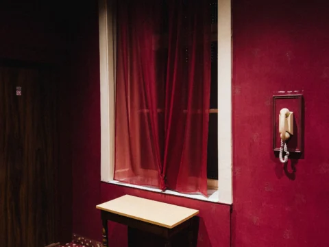Intérieur aux murs rouges avec une fenêtre voilée et un téléphone mural
